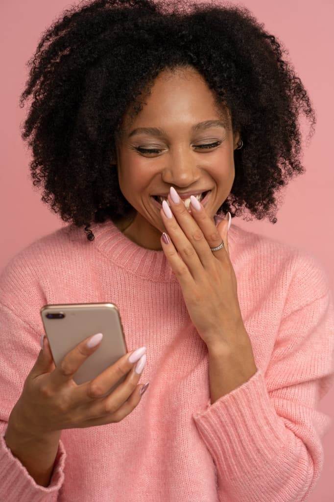 Smiling young Afro woman looking at mobile phone laughing at joke watch funny video on smartphone.